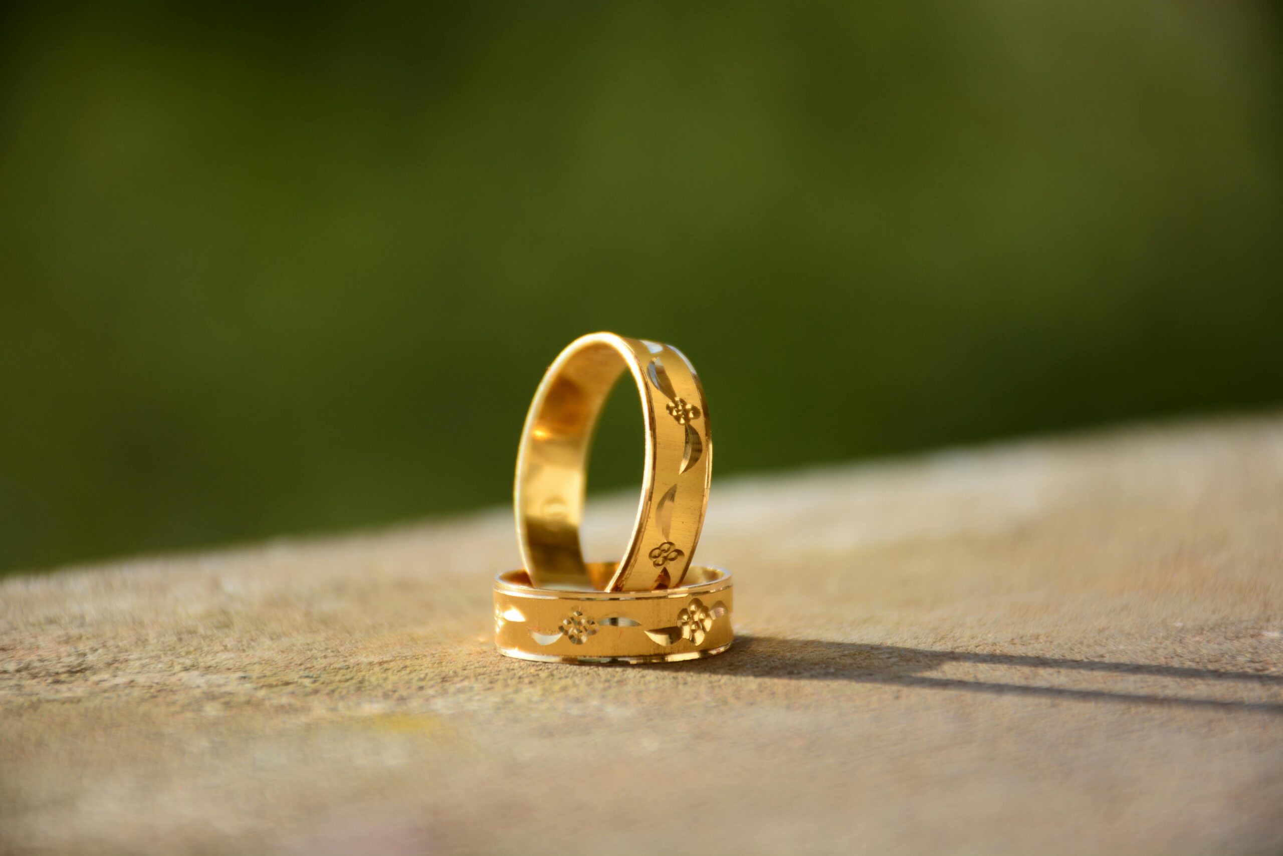 Close-up of two decorative gold wedding rings casting shadows on a warm surface.